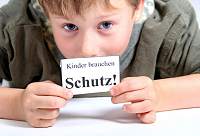 Ein Junge hält einen Zettel in die Kamera. Aufschrift: "Kinder brauchen Schutz!"