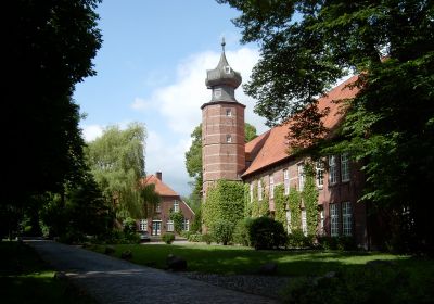 Burg Kniphausen mit Zwiebelturm umgeben vom Grün der Parkanlage an einem sonnigen Tag.