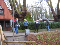 5 Personen, teilweise mit Schreibblöcken und ähnlichen Unterlagen in der Hand, stehen einander zugewandt auf dem Weg vor dem Bootshaus.