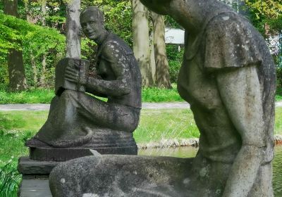 Steinfiguren "Hein und Grete", die sich über mehrere Sitzbänke hinweg ansehen.
