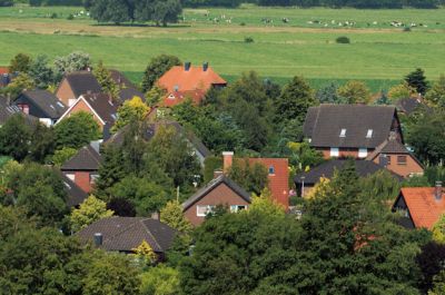 Blick über ein Wohngebiet mit vielen Bäumen und Sträuchern. Direkt dahinter beginnt eine weitläufige Wiese.