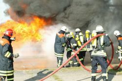 Feuerwehrmänner in Schutzkleidung löschen einen Brand mit viel dunklem Rauch