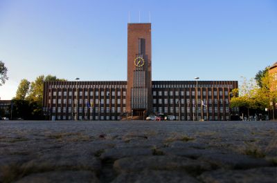 Das Rathaus früh am Morgen in der Frontalansicht aus nördlicher Richtung, aufgenommen dicht über das Pflaster des Rathausplatzes hinweg.