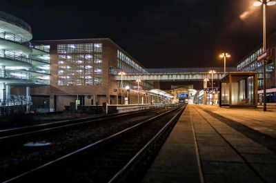 Der Bahnhof Wilhelmshaven bei Nacht, aufgenommen entlang der Bahnsteigkante und umgeben von den Lichtern der Nordseepassage.