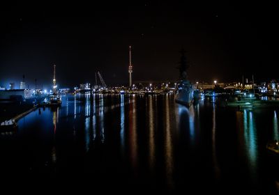 Nächtlicher Blick von der KW-Brücke in Richtung des Marinemuseums mit zahlreichen Lichtern, die sich im Wasser spiegeln..