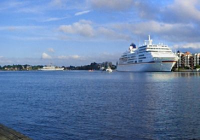 Blick über den Großen Hafen. Im Vordergrund ein Holzsteg mit einem Segelboot. Im Hintergrund am Bontekai ein weißes Kreuzfahrtschiff.