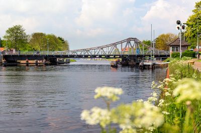 Deichbrücke an einem sommerlichen Tag. Aufgenommen aus Richtung des Großen Hafens über die Blüten der Pflanzen an der Uferböschung.